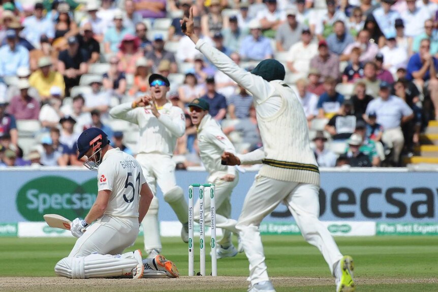 England batsman Jonny Bairstow is on his knees while Australian fielders shout about his dismissal during a Test.