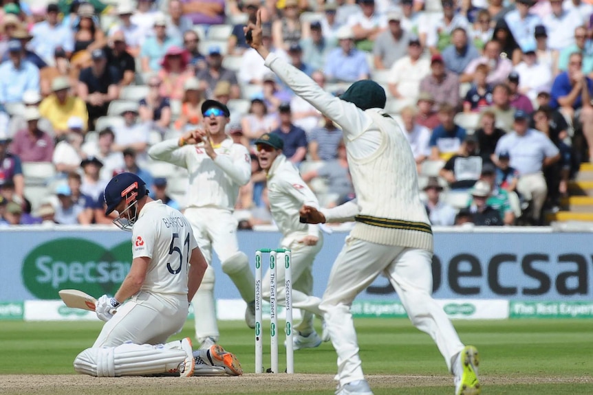 England batsman Jonny Bairstow is on his knees while Australian fielders shout about his dismissal during a Test.