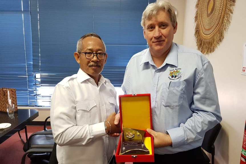 Two men presenting a trophy in an office.