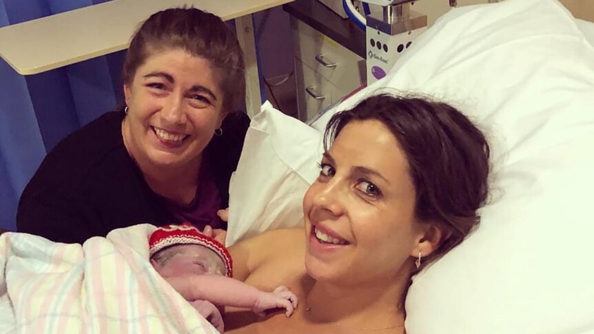 Kylie Coad sitting beside hospital bed smiling, with Jenny Clearihan holding newborn baby on her chest