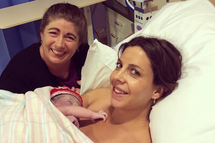 Kylie Coad sitting beside hospital bed smiling, with Jenny Clearihan holding newborn baby on her chest.