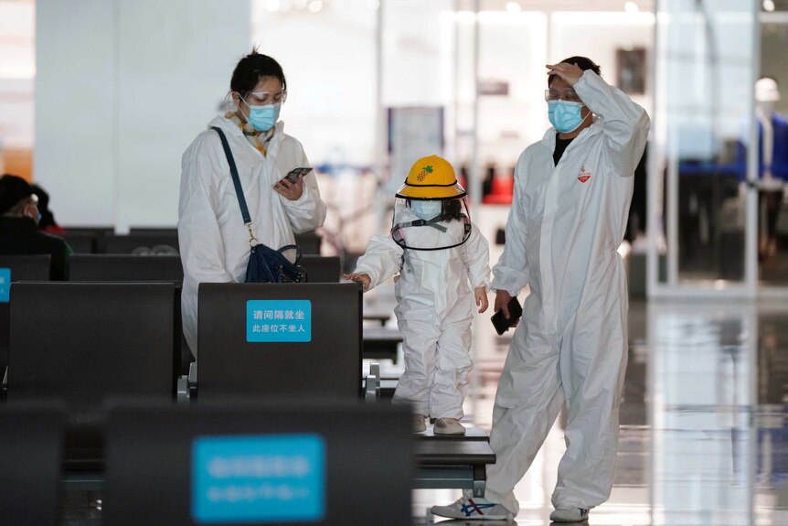 Two adults and a child in full protective suits at an airport.