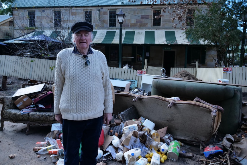 An old man stands outside an historic pub next to a pile of garbage.