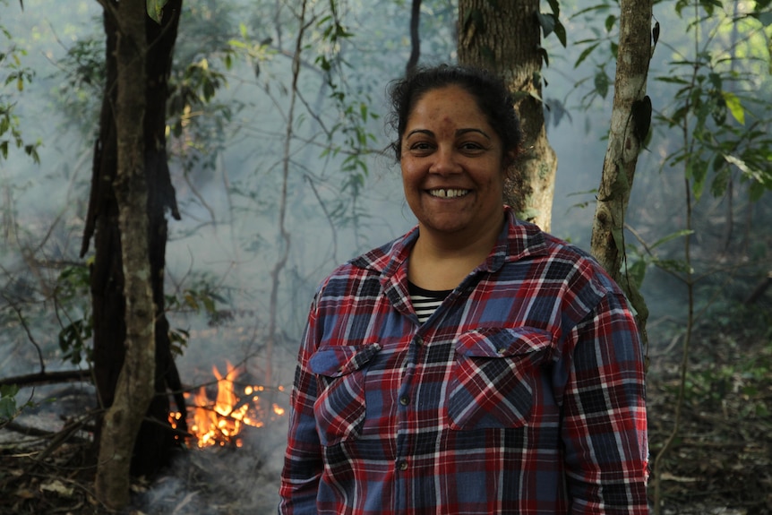 A woman smiles for the camera with a small fire in the background.