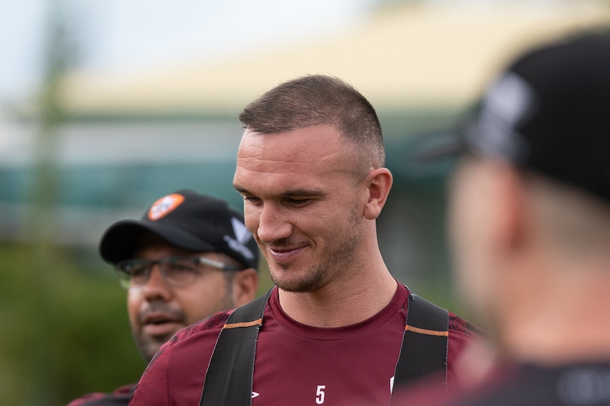 Brisbane Roar captain Tom Aldred, wearing a Brisbane Roar jersey, smiles and looks to his right at a training session.