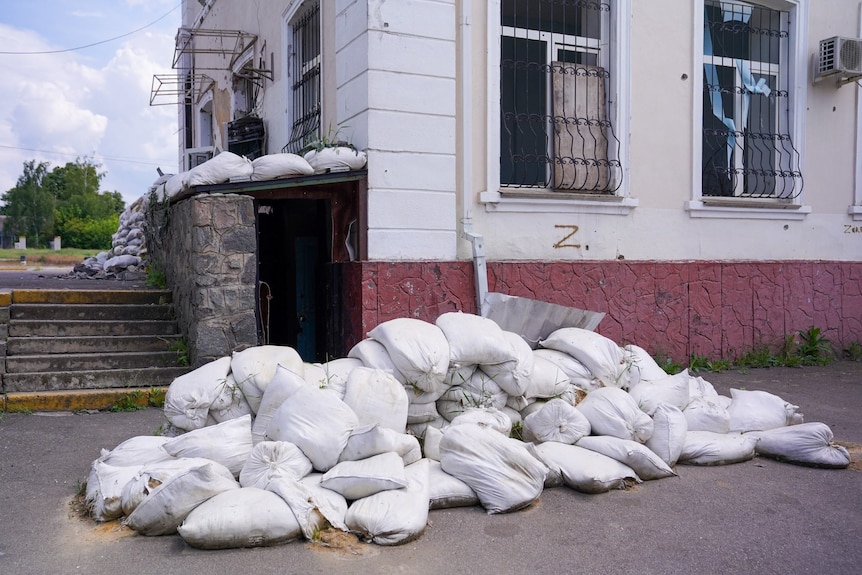 A small, dark entryway is protected by a pile of sandbags. There is a Z graffiti on the brick wall next to the open door.