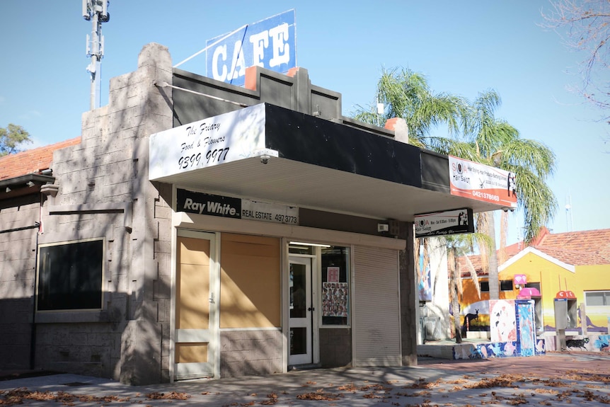 A boarded up shop neighbours a hairdresser with an old cafe sign on the room