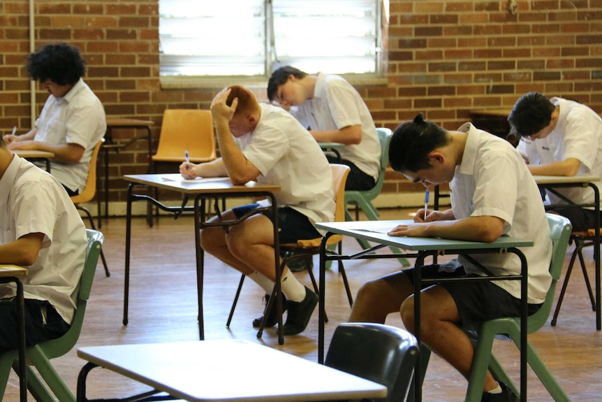 High school boys sitting at desks in a school gymnasium sitting a school exam.