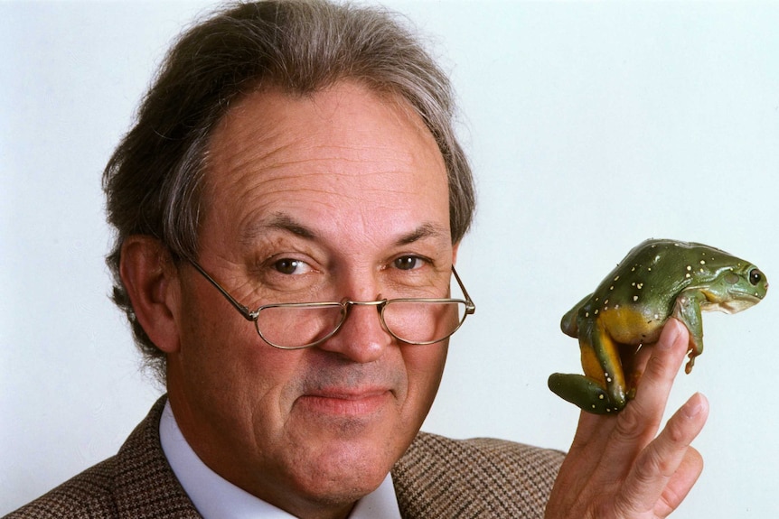 A man of late middle age, bespectacled and conservatively dressed, holding a frog.