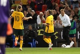 A delighted football coach yells from the sideline as his players smile at each other after a goal.