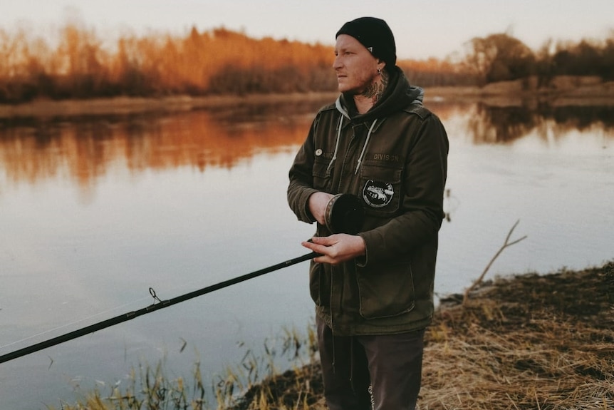 A fisherman standing next to the sea with his fishing rot in Latvia.