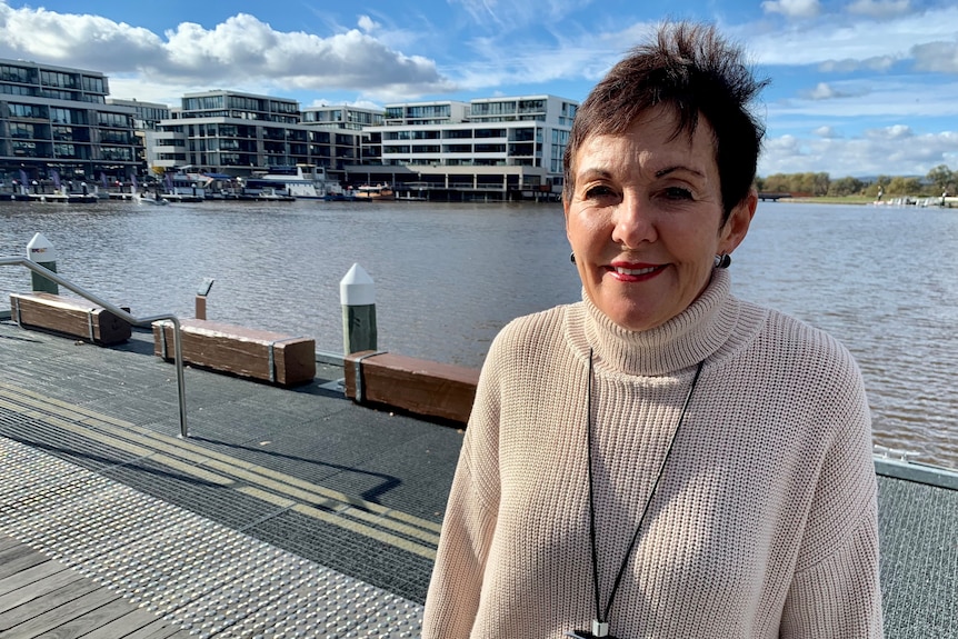 Woman wearing white knit jumper standing beside a lake. 