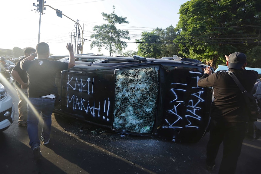 Plain-clothed police officers secure the area where a government-owned car is overturned
