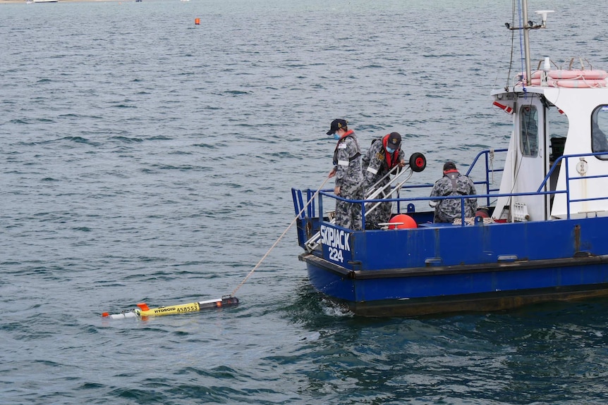 Two people stand on a boat pulling an autonomous underwater vehicle on board.