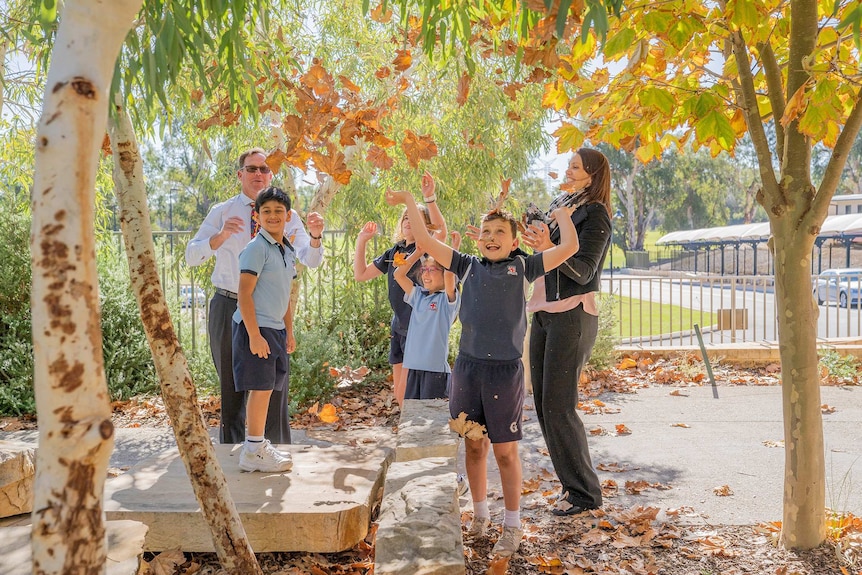 Guilford Grammar Preparatory School head Clark Wight and deputy head Holly Miller stand throwing leaves with four students.