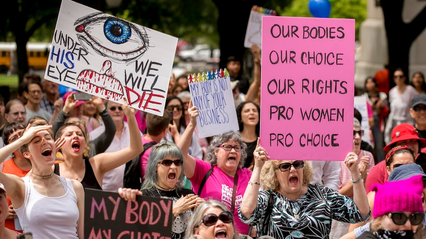 A group of mostly women shout and wave pro-choice banners at a protest against restrictive abortion laws.