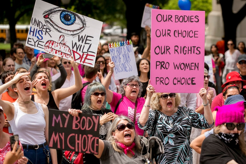 A group of mostly women shout and wave pro-choice banners at a protest against restrictive abortion laws.