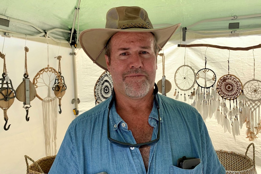 A man in a hat stands in a tent with wind catchers behind him.