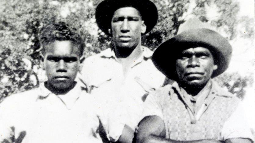 Three men in old fashioned clothes, two at the front and one at the back, one of them has arms folded.