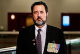 Former Australian serviceman Simon Marshall stands dressed in a suit, wearing his medals.
