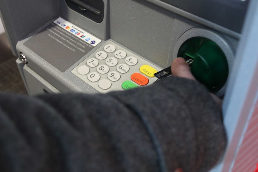 A man puts a bank card into an ATM machine.