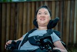 Melanie Tran sits in her wheelchair in front of a wooden fence.