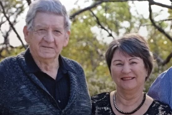 Middle aged man and woman couple standing together, portrait photo, in front of trees.