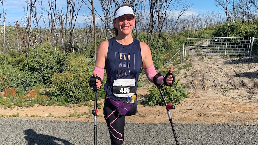 Woman amputee stands on road wearing marathon clothes, with scrub in background