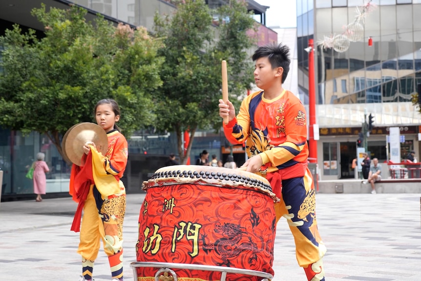 A young boy plays a drum in a public square