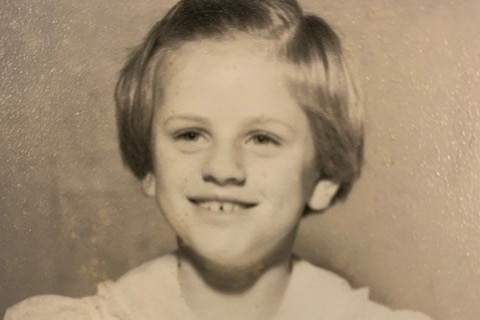 Black and white photo of a young girl smiling with large ribbon on top of her head.