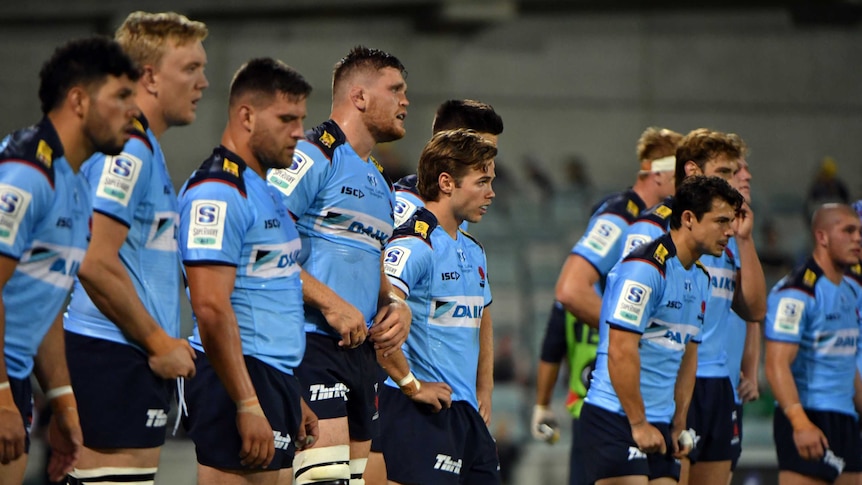 Waratahs players stand in a row looking tired after the Brumbies score a Super Rugby try against them.