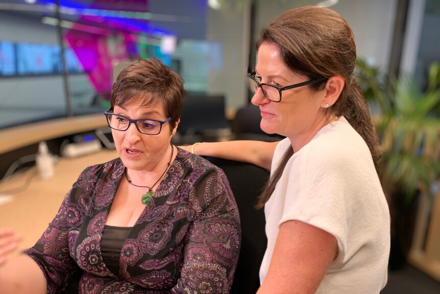 Niki Petousis, delivery lead at Telstra sits at a workstation with Alex Badenoch standing next to her.