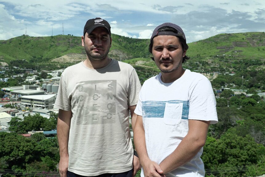 Samar and Zalman stand on a hill in Port Moresby with buildings behind them below