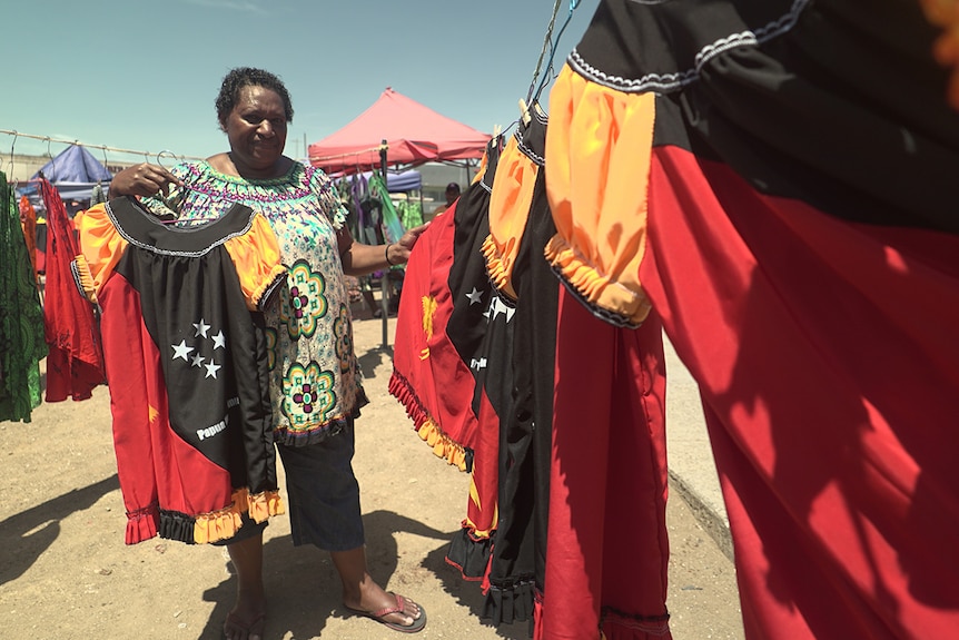 Market vendor Regina Robert with meri blouses she has made in PNG's flag colours.