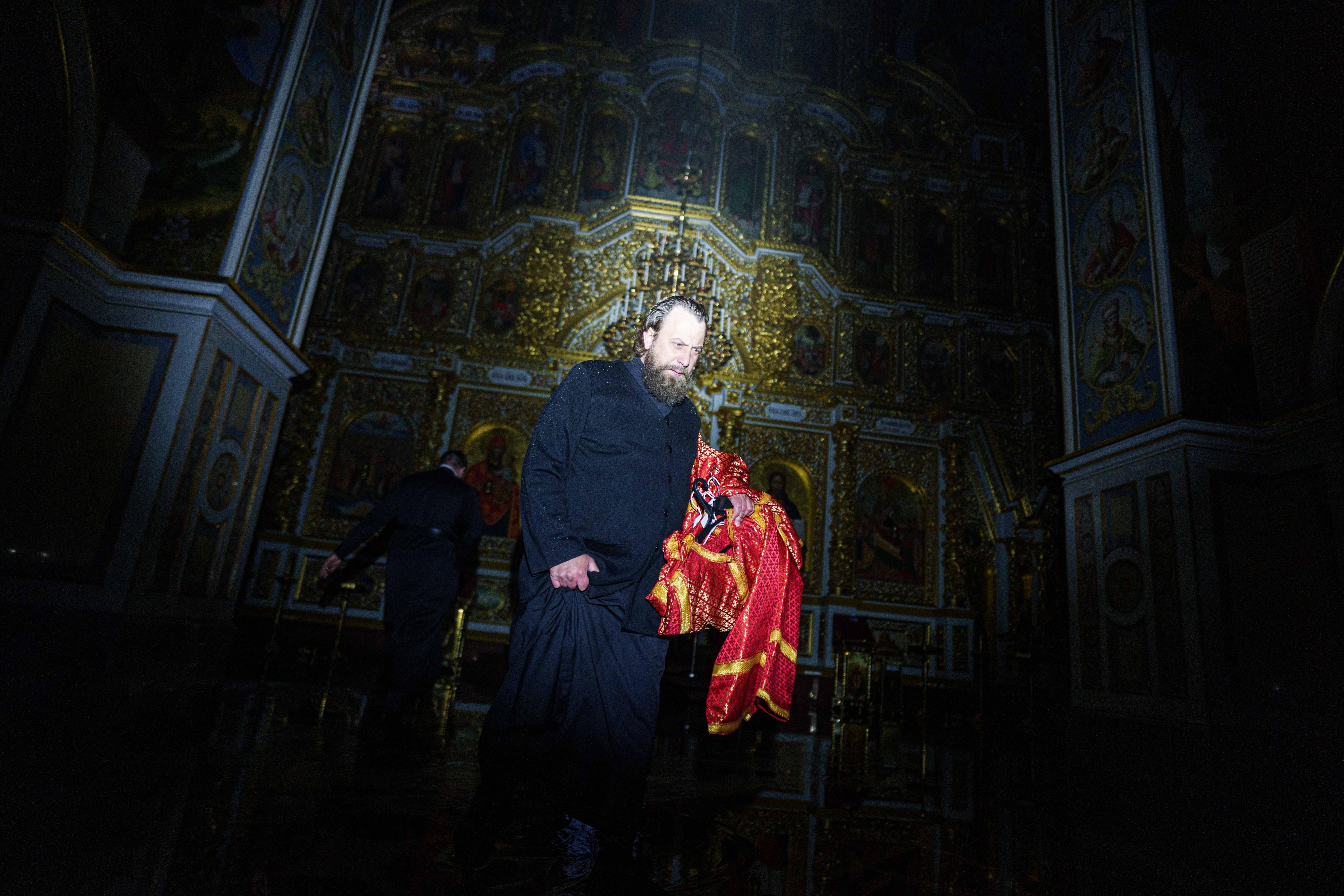 A bishop walks through a dark cathedral damaged in a fire carrying church inventory.