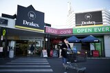 A woman waling behind a trolley in front of a Drakes Supermarkets store