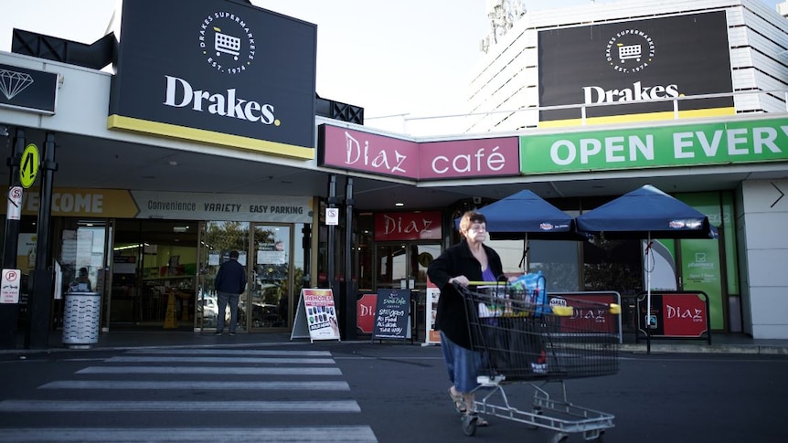 A woman waling behind a trolley in front of a Drakes Supermarkets store