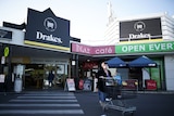 A woman waling behind a trolley in front of a Drakes Supermarkets store