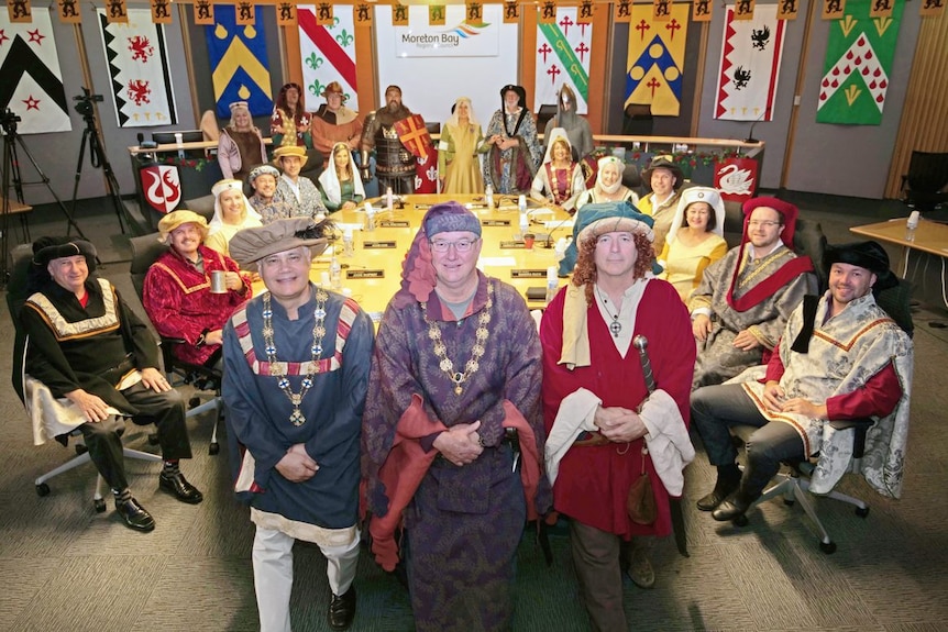 Members of the Moreton Bay Regional Council dressed in medieval garb sit around a table in the council chambers. 