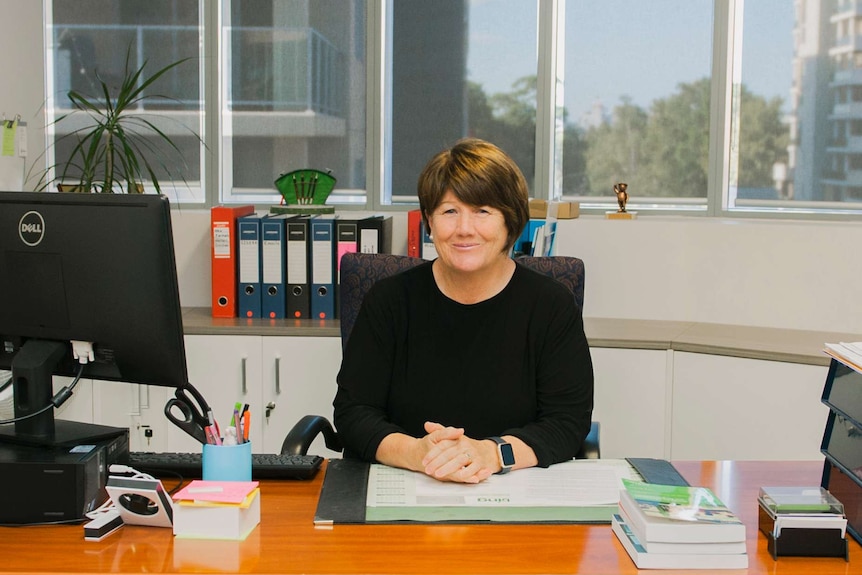 A woman with short hair sitting at her desk with a computer and folders.