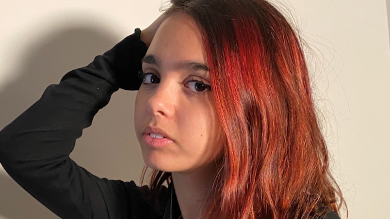 An Aboriginal teenager with one arm on her head and the other holding a camera