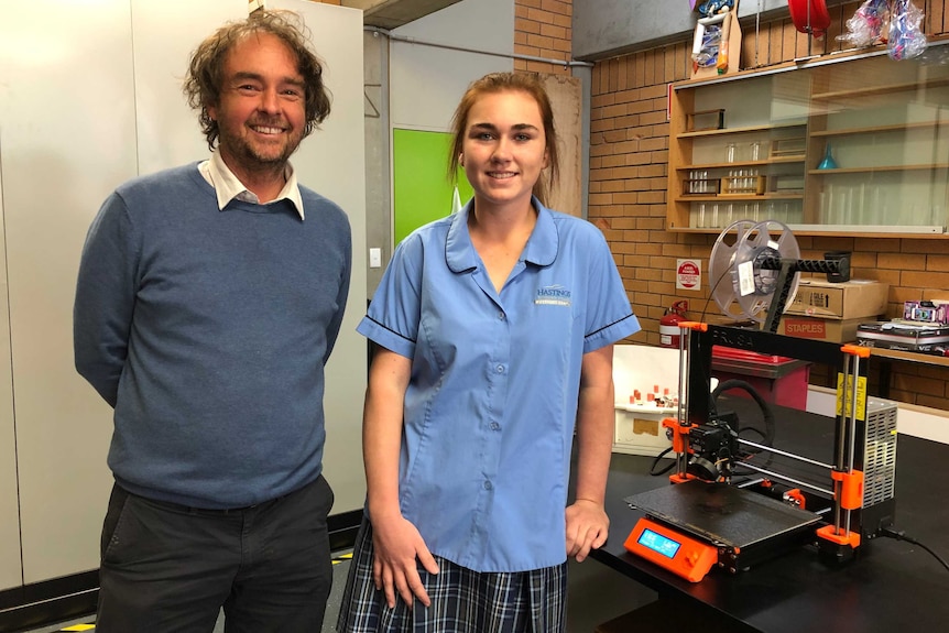 A teacher and student standing with a 3D printer.