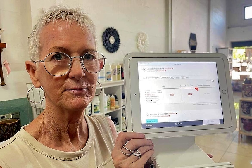 A woman with a concerned expression gestures to a flight booking webpage open on a computer screen