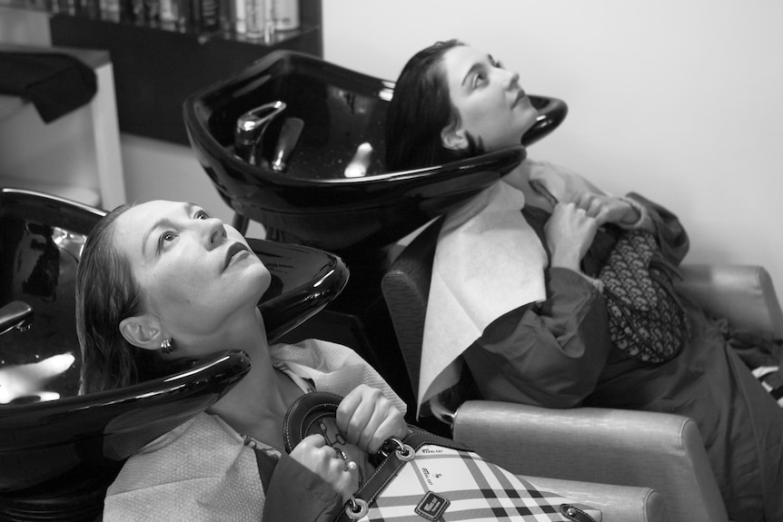 A black and white image of mother and daughter lying back in hairdresser's basins