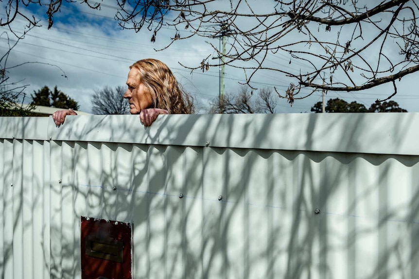 Donna Dickson stands behind a high fence, looking over.