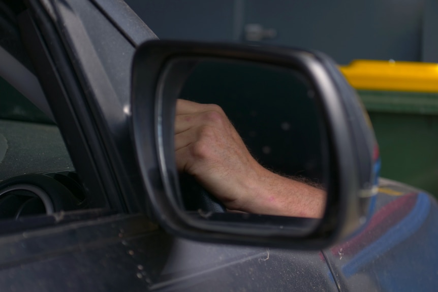 A car door's window. In the reflection there is a hand on the wheel