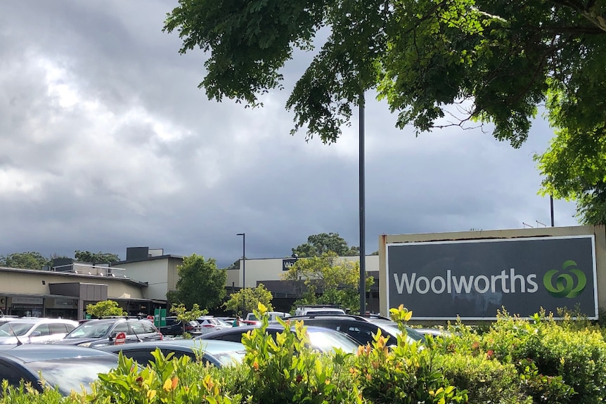 The outside of a large supermarket sign with trees and full car park of cars