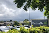 The outside of a large supermarket sign with trees and full car park of cars