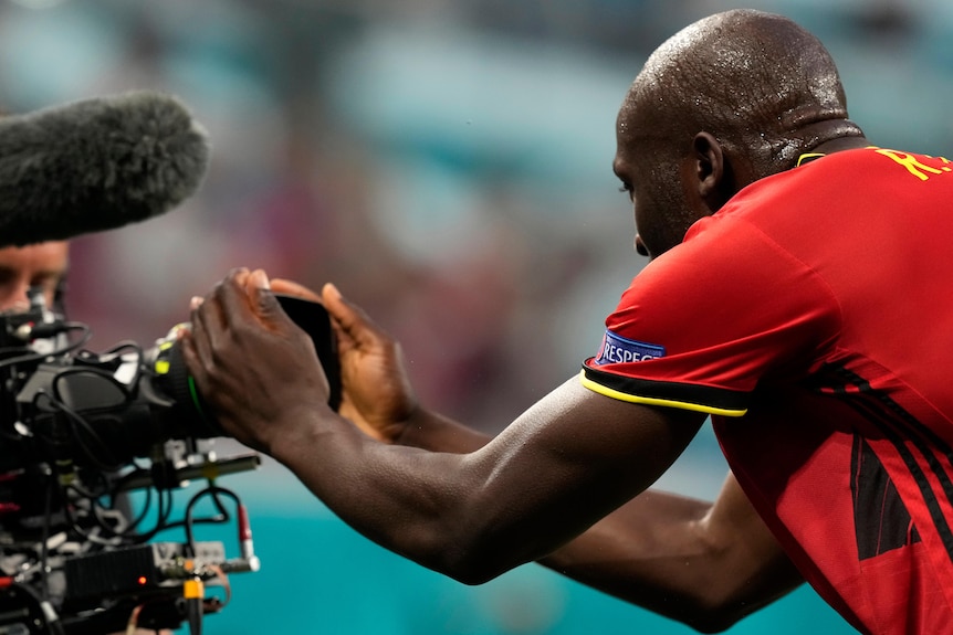 Romelu Lukaku bends forward and holds a camera in both hands
