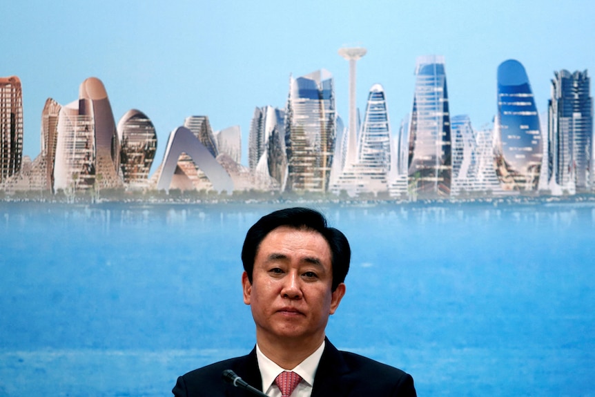 A Chinese businessman in a suit in front of a background full of tall apartments in China.